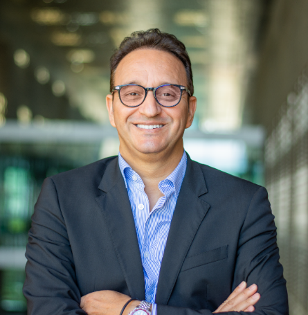 Portrait of Mohamed Eddaoudi, smiling, in glasses and a dark jacket, arms folded.